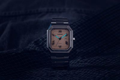 Monarch salmon dial automatic watch displaying luminous hands and markers in low light conditions